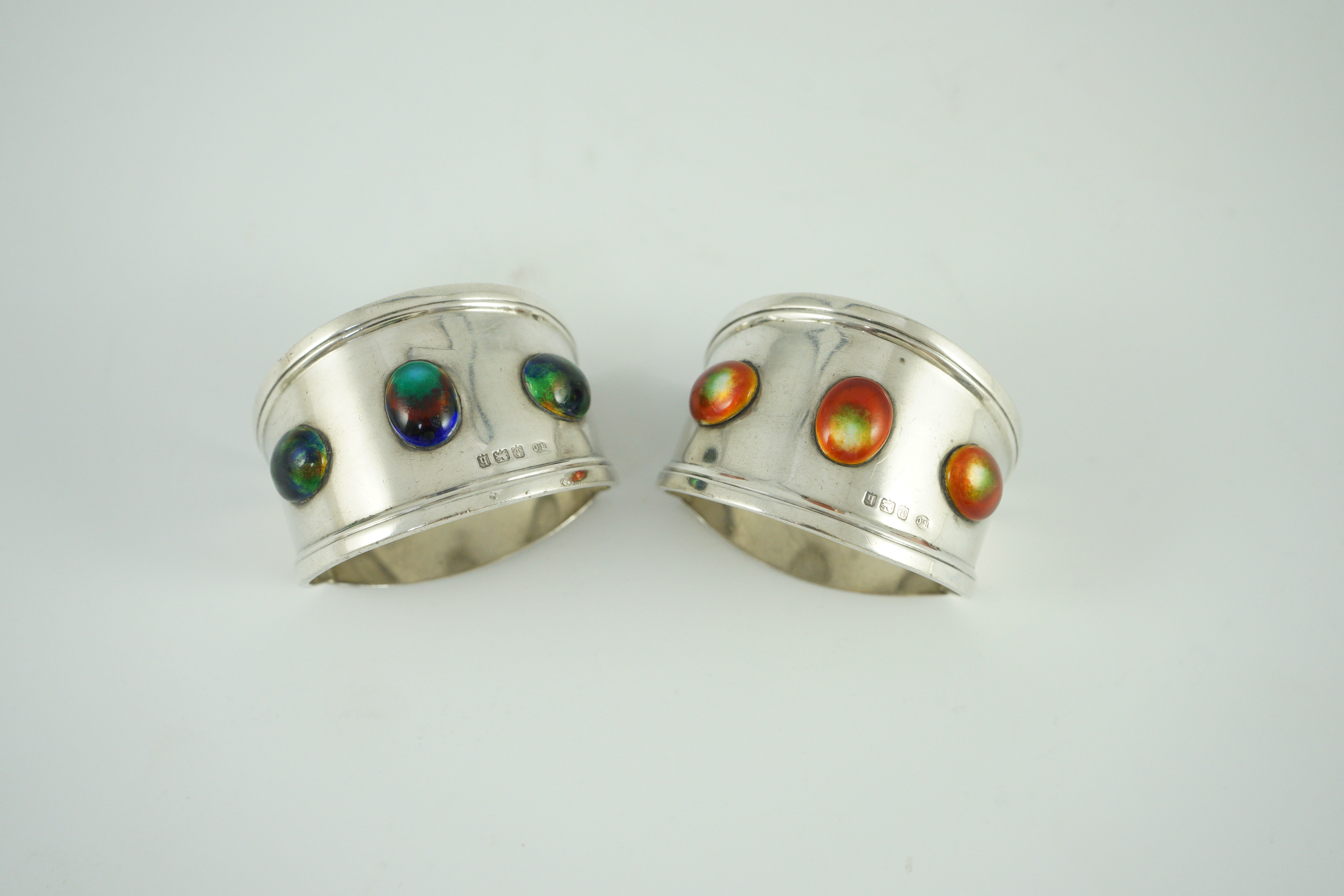 Two similar Edwardian Arts & Crafts silver and enamelled napkin rings